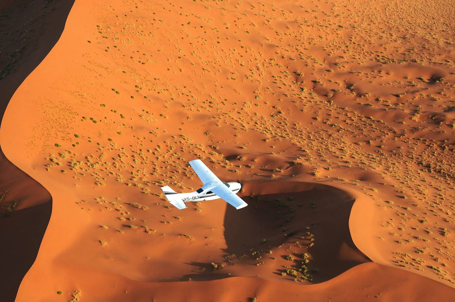 Ein Kleinflugzeug über den orangefarbenen Dünen einer Wüstenlandschaft